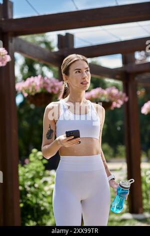 Une jeune femme atteinte de vitiligo, vêtue de vêtements actifs blancs, vérifie son téléphone en marchant dans un parc. Banque D'Images