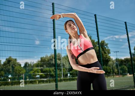 Une jeune femme atteinte de vitiligo s'étire à l'extérieur dans un soutien-gorge de sport rose et des leggings noirs. Banque D'Images