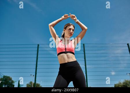 Une jeune femme atteinte de vitiligo, portant un soutien-gorge de sport rose et des leggings noirs, s'étire dans un parc extérieur. Banque D'Images