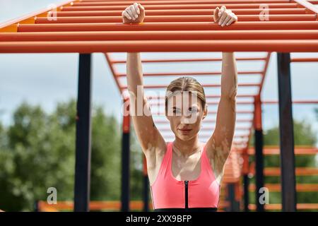 Une jeune femme atteinte de vitiligo en sportswear rose est suspendue à un bar à singes dans un gymnase en plein air. Banque D'Images