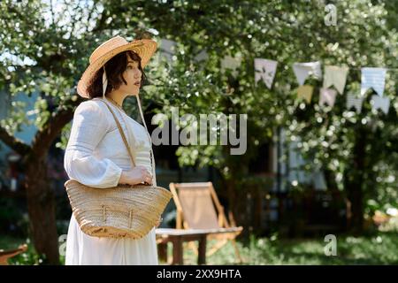 Une jeune femme dans une blouse blanche et un chapeau de paille marche dans un jardin d'été luxuriant, portant un sac Banque D'Images