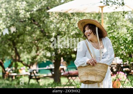 Une femme dans une blouse blanche et un chapeau de paille sourit brillamment alors qu'elle marche dans un jardin ensoleillé. Banque D'Images