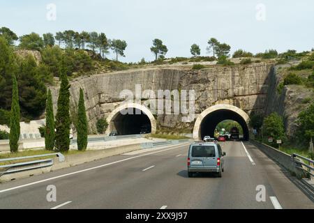 Nice, France - 6 juin 2023 : une route à voie unique traverse deux tunnels creusés dans une colline rocheuse, avec une camionnette se dirigeant vers les tunnels et Banque D'Images