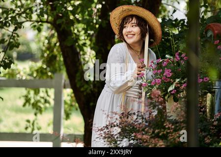 Une jeune femme dans une robe blanche et un chapeau de paille sourit tout en s'occupant d'un jardin de fleurs vibrant par une journée d'été ensoleillée. Banque D'Images