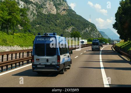 Ossenigo, Italie - 8 juin 2023 : les forces de l'ordre se déplacent sur une autoroute très fréquentée, flanquée de verdure luxuriante et de montagnes imposantes sous un bleu clair Banque D'Images