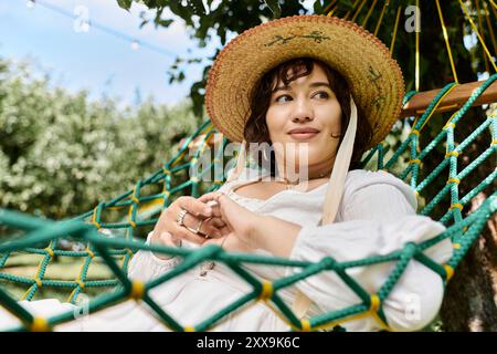 Une femme se détend dans un hamac par une journée d'été ensoleillée, profitant de la paix et de la tranquillité de son jardin. Banque D'Images