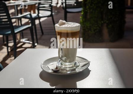 Caffe latte en couches dans un grand verre sur la table dans un café dans la rue. Arrière-plan flou, pas de gens. Banque D'Images