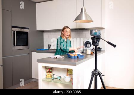Jeune femme enregistrant un blog vidéo avec un téléphone intelligent à la maison dans la cuisine faisant des croissants. Banque D'Images