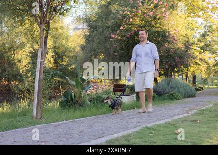 Souriant homme d'âge moyen marche et joue avec un petit chien dans un parc public Banque D'Images