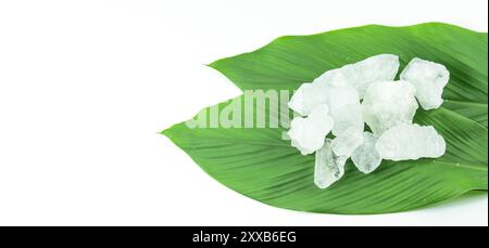 Cubes d'alun clairs et immaculés reposant dans un panier en bambou à côté des feuilles, sur un fond blanc, mettant en valeur la pureté naturelle et la tradition Banque D'Images