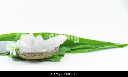 Cubes d'alun clairs et immaculés reposant dans un panier en bambou à côté des feuilles, sur un fond blanc, mettant en valeur la pureté naturelle et la tradition Banque D'Images