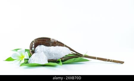 Cubes d'alun clairs et immaculés reposant dans un panier en bambou à côté des feuilles, sur un fond blanc, mettant en valeur la pureté naturelle et la tradition Banque D'Images