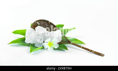 Cubes d'alun clairs et immaculés reposant dans un panier en bambou à côté des feuilles, sur un fond blanc, mettant en valeur la pureté naturelle et la tradition Banque D'Images