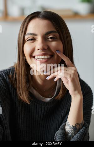 Une jeune femme aux cheveux bruns et un pull gris sourit en travaillant à domicile. Banque D'Images