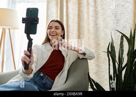 Une jeune femme, en tenue décontractée, enregistre une vidéo, souriant brillamment alors qu'elle utilise un stabilisateur de téléphone. Banque D'Images