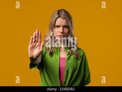 Jeune femme élégante désapprouvant avec le signe de main de paume d'arrêt. Ne jouez pas avec moi, assez. Portrait de dame sur fond jaune. Haute qualité Banque D'Images