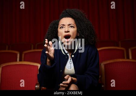 Une jeune femme est assise dans un siège de cinéma, la bouche agape, réagissant au film qui joue sur l'écran. Banque D'Images