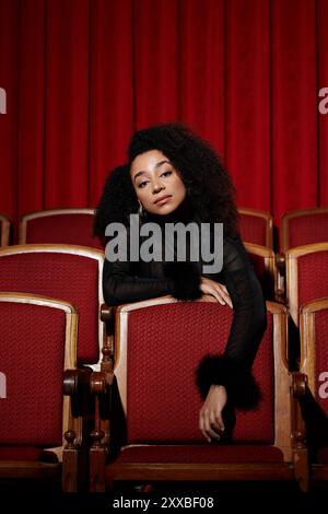 Une femme élégante dans une tenue noire est assise dans un siège de cinéma en velours rouge, engrossée dans un film. Banque D'Images