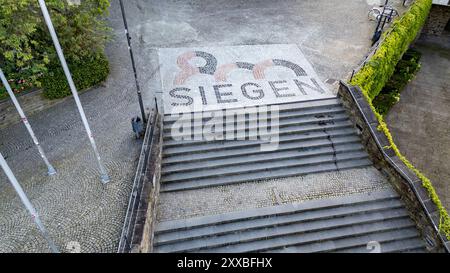 Luftaufnahme. Die Stadt Siegen wird 2024 800 Jahre alt. Zu diesem Anlass wurden am Treppenaufgang zur Nikolaikirche und zum Rathaus Naturpflastersteine mit dem Siegen 800 logo verlegt. Die Pflastersteine wurden vom AWZ Bau Aus- & Weiterbildungszentrum durch sieben Auszubildende verschiedener Firmen verlegt und sind ein Geschenk zum Stadtjubilaeum Stadtjubiläum. Sommer im Siegerland AM 22.08.2024 à Siegen/Deutschland. *** Vue aérienne la ville de Siegen aura 800 ans en 2024 pour marquer l'occasion, des pavés naturels avec le logo Siegen 800 ont été posés à l'escalier du Nikolai CH Banque D'Images