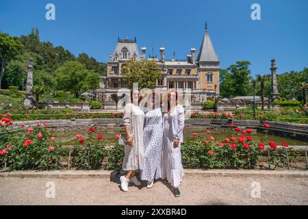 Trois femmes posant devant une grande maison avec un jardin Banque D'Images