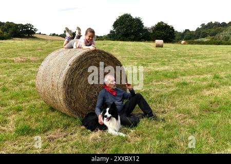 Amusement en famille sur la ferme grand-parent et petit-enfant avec le chien Border Collie sur la balle de foin Shropshire, Angleterre, Grande-Bretagne, Royaume-Uni Banque D'Images