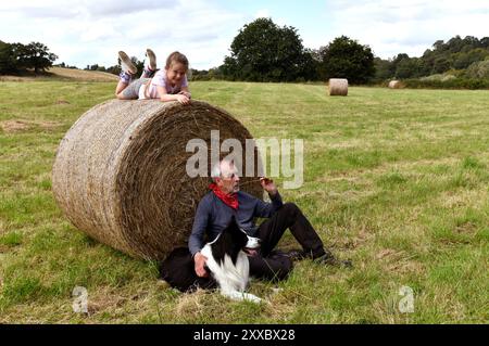 Amusement en famille sur la ferme grand-parent et petit-enfant avec le chien Border Collie sur la balle de foin Shropshire, Angleterre, Grande-Bretagne, Royaume-Uni Banque D'Images