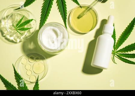Feuilles de cannabis de chanvre et produits cosmétiques, huile de cbd dans une boîte de Petri, crème pour le visage et sérum sur fond vert clair, vue de dessus. Bio recherche et bio Banque D'Images