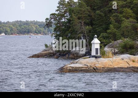 Une vue panoramique d'un phare sur une rive rocheuse, entouré d'arbres et d'eau. Le phare est blanc avec une base noire, debout sur un gros rocher. Po Banque D'Images