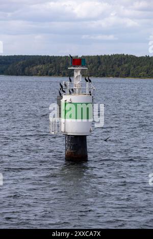 Un phare vert et blanc se dresse dans l'eau, entouré d'arbres en arrière-plan. Plusieurs oiseaux sont perchés au sommet du phare, avec un cl Banque D'Images