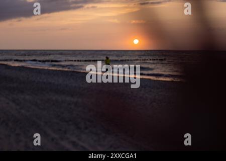 Strand von Warnemünde an der Ostsee Sommer 2024 Warnemuende, Deutschland 23. Août 2024 : Die hand eines Kindes ist im Vordergrund zu sehen während eine Frau den Sonnenuntergang am Strand von Warnemünde an der Ostsee in Deutschland im Sommer 2024 geniesst.. Mecklembourg-Poméranie occidentale Banque D'Images