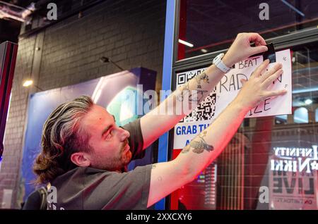 Cologne, Rhénanie du Nord-Westphalie, Allemagne. 23 août 2024. Un employé sur un stand pose une pancarte annonçant un prix si un participant à la Gamescom peut battre un streamer connu sous le nom de RADAHN (non représenté sur la photo) dans le centre de congrès Koelnmesse à Cologne, Rhénanie du Nord-Westphalie, Allemagne, le 23 août 2024. Gamescom est le plus grand salon de jeux vidéo au monde. (Crédit image : © Kai Dambach/ZUMA Press Wire) USAGE ÉDITORIAL SEULEMENT! Non destiné à UN USAGE commercial ! Banque D'Images