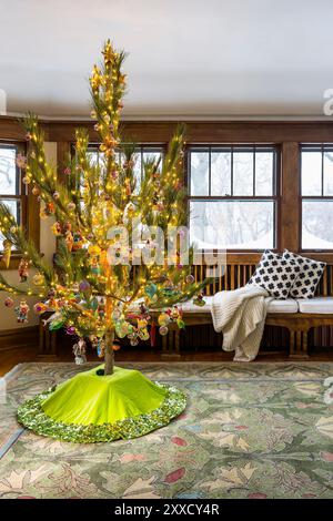 Arbre de Noël installé dans la chambre avec banc intégré sous les fenêtres avec vue sur la neige et les arbres d'hiver Banque D'Images