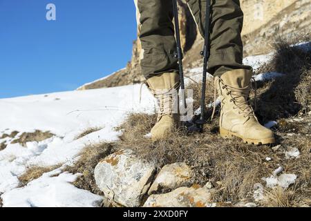 Gros plan du pied d'un touriste en bottes de trekking avec des bâtons pour la marche nordique debout sur une pierre dans les montagnes caucasiennes Banque D'Images