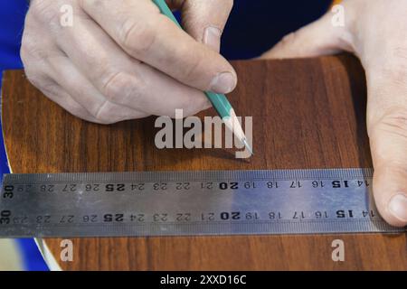 Gros plan les mains des hommes dessinent un crayon sur la règle avec un modèle de qualité inférieure pour découper les détails du meuble à côté de la scie sauteuse et des clips de meubles Banque D'Images