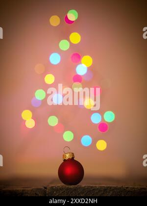 Gros plan d'une boule de Noël rouge sur une table de bois, du flou des lumières d'arbre de Noël en arrière-plan, beau bokeh Banque D'Images