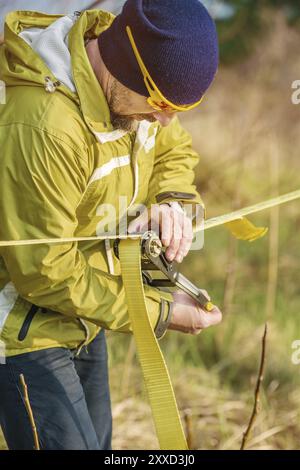 Gros plan Un homme ajuste le slackline de l'équipement avant d'effectuer des tours de slackline fous et de marcher sur un slacklin dans un parc dans la nature Banque D'Images