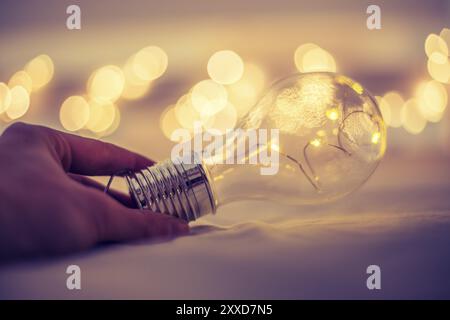 L'ampoule LED est couchée dans le lit, les mains se touchant. Symbole des idées et de l'innovation. Spot lumières dans l'arrière-plan flou Banque D'Images