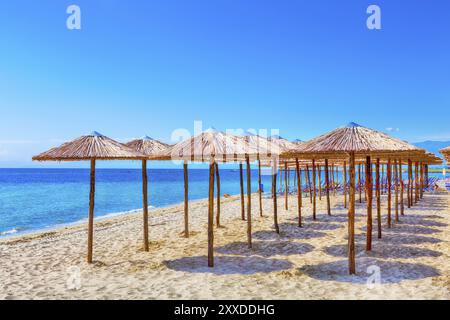 Rangée de parasols en bois à la plage de sable, fond de vacances de mer et de ciel bleu, Grèce, Europe Banque D'Images