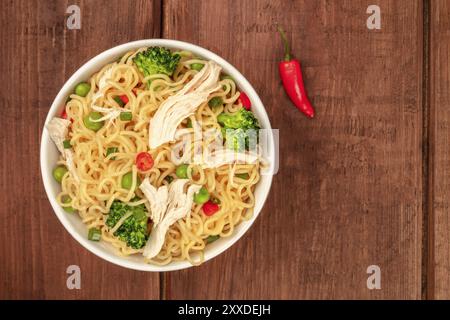 Nouilles au poulet, aux pois verts et au brocoli, avec un piment rouge, tirées du haut sur un fond de bois rustique foncé avec une place pour le tex Banque D'Images