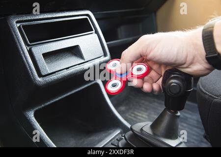 Gros plan de la main d'un homme jouant avec un spinner alors que dans un embouteillage sur un levier de changement de vitesse d'une boîte de vitesses de voiture jouet populaire spinner fidget Banque D'Images