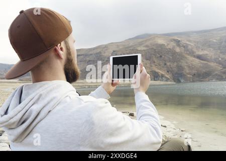 Personne hipster tenant dans les mains tablette numérique avec écran vide blanc, photographie de l'homme sur ordinateur sur fond nature paysage extérieur maquette technique Banque D'Images