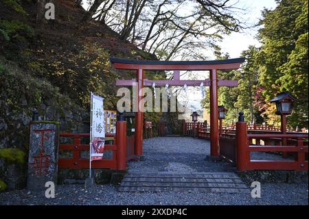 Vue panoramique d'une ancienne porte Shinto Torii en bois laqué vermillon à l'entrée du pont Shinkyō, traversée d'une rivière sacrée à Nikkō, Japon. Banque D'Images