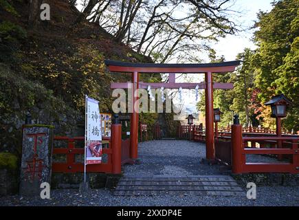 Vue panoramique d'une ancienne porte Shinto Torii en bois laqué vermillon à l'entrée du pont Shinkyō, traversée d'une rivière sacrée à Nikkō, Japon. Banque D'Images