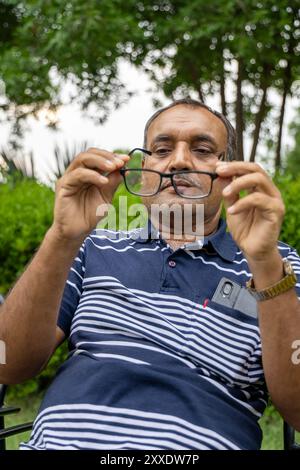 homme isolé nettoyant ses lunettes au parc extérieur le soir à partir d'un angle plat Banque D'Images