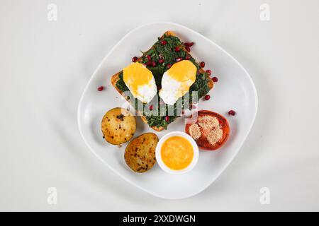 Pain grillé sain avec épinards, œufs frits, graines de grenade et épinards frais. Délicieux petit déjeuner ou collation isolé sur fond blanc Banque D'Images