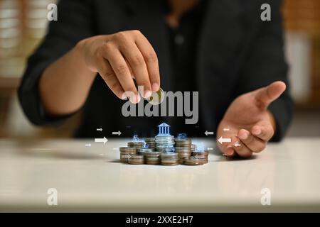 Homme plaçant une pièce de monnaie sur le dessus de la pile de pièces de monnaie avec diverses icônes financières. Transactions financières, épargne et concept d'investissement Banque D'Images