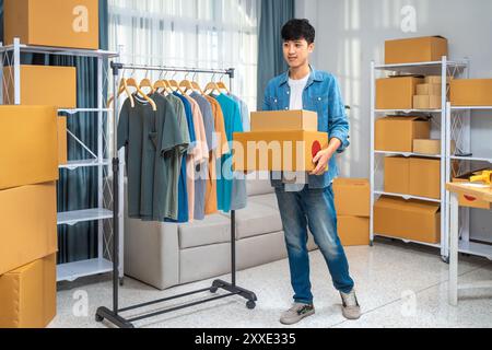 Heureux jeune homme vendeur en ligne tenant ses boîtes de produits emballées pour envoyer à son client Banque D'Images