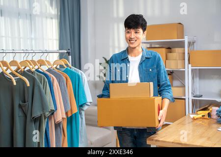 Heureux jeune homme vendeur en ligne tenant ses boîtes de produits emballées pour envoyer à son client Banque D'Images