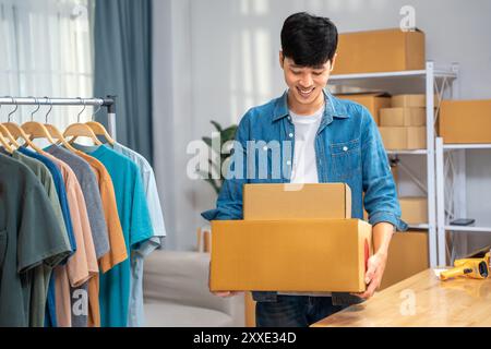 Heureux jeune homme vendeur en ligne tenant ses boîtes de produits emballées pour envoyer à son client Banque D'Images