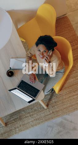Une femme travaille efficacement de la maison en utilisant son ordinateur portable pendant un appel téléphonique Banque D'Images